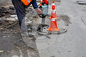 A road worker smashes asphalt with an electric jackhammer around a sewer hatch on the road