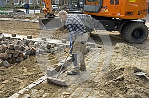 Road worker sweeps sand between cobblestones