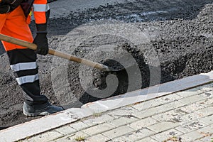 Road worker in uniform with a shovel, throwing wet gravel. Asphalt roads. Road works