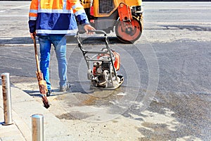 A road worker uses a gasoline vibratory compactor, a vibratory roller and an old broom to repair the road
