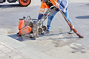 A road worker uses a petrol vibratory compactor, a vibratory roller, and an old broom to compact the asphalt on a stretch of road