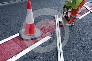 Road workers applying hot melt traffic resistant paint for white, yellow and red road marking lines on new build asphalt road