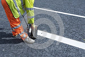 Road workers applying hot melt traffic resistant paint for white, yellow and red road marking lines on new build asphalt road