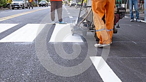 Road workers group with thermoplastic spray marking machine are painting pedestrian crosswalk on asphalt road