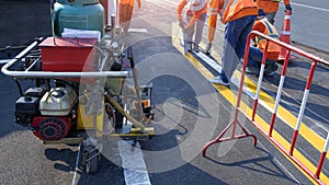 Road workers group with thermoplastic spray road marking machine are working to paint traffic lines on asphalt road