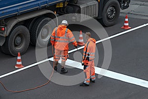 Road workers in orange uniforms renovate road markings