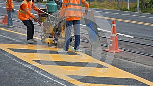 Road workers with thermoplastic spray road marking machine are working to paint traffic yellow lines