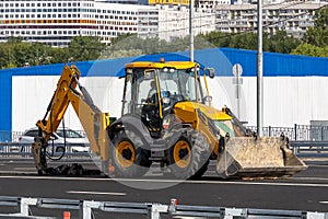 Road works in the city. A yellow wheeled tractor breaks asphalt with a jackhammer to install dividing fences between