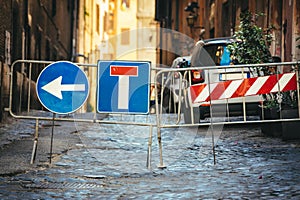 Road works detour road signs. Dead end road and arrow to turn left. Iron crossing barrier. Street with paving cobblestones