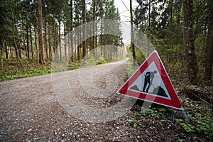 Road works or men at works tringle sign on the side of a forest road in Europe. Trees in the background, no people, dirt road