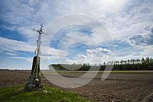 Roadside cross on plowed field.