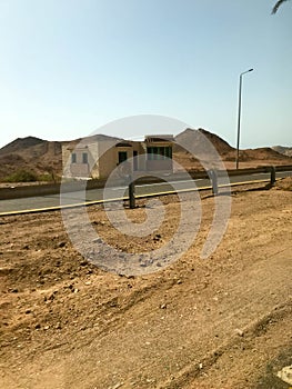 The roadside, road with asphalt in the desert with sand, bumpers and lampposts, sand dunes, hills, mountains and houses in a hot t