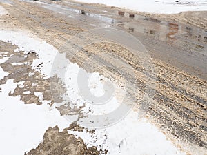 Roadside with a snowdrift. Difficult driving conditions. Wet slippery pavement with footprints. Dangerous ice. Muddy