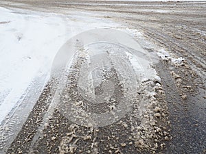 Roadside with a snowdrift. Difficult driving conditions. Wet slippery pavement with footprints. Dangerous ice. Muddy