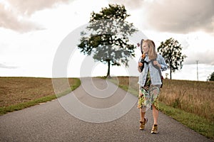 Roadside stroll. Girl with a longboard on her back.