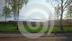 Roadway out of town. Plowed field, trees on background. Highway along rural area. View through right side window on