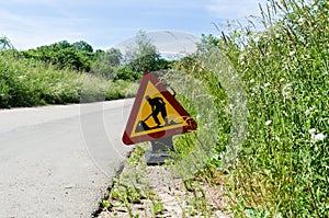 Roadwork sign by roadside among green grass