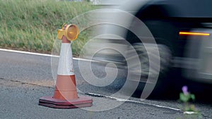 Roadworks cone flashing on UK motorway at night with traffic passing