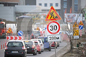 Roadworks warning traffic signs of construction work on city street and slowly moving cars