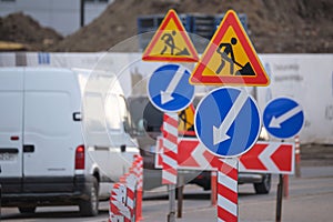 Roadworks warning traffic signs of construction work on city street and slowly moving cars