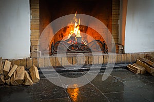 A roaring fire within a large stone arched fireplace, with pile of logs.