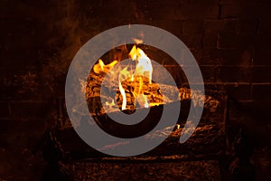 A roaring indoor fire with orange flames in a wood burning fireplace with metal fireback fireplace grate