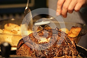 Roast beef with meat thermometer next to pan of roasted potatoes