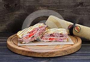 Roast beef panini with tomato, onion and cheese on a round cutting board
