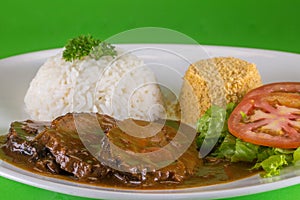 Roast beef with rice and salad on the green background is a traditional dish of Brazilian cuisine