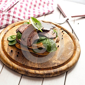 Roast beef sandwich with salad and pepper on rustic wooden plate.