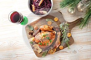 Roast chicken with fruits and herbs, red cabbage and wine on a wooden board, pine branches and Christmas decoration, holiday