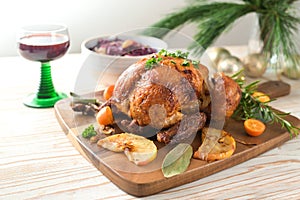 Roast chicken from the oven with fruits and herbs, served with red cabbage and wine on a wooden board, pine branches and Christmas