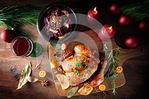Roast chicken with red cabbage and wine on dark rustic wood with candles and Christmas decoration, festive poultry dinner for