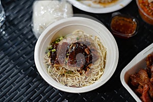 Roast duck noodles in a foam bowl on a black rattan table photo