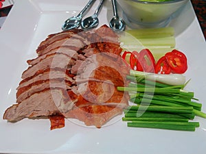 Roast duck on a plate with veggies and white sauce.