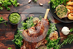 Roast Lamb leg with mint sauce, rosemary and garlic. on black plate, wooden table