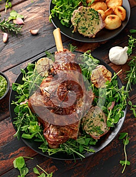 Roast Lamb leg with mint sauce, rosemary and garlic. on black plate, wooden table