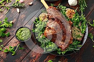 Roast Lamb leg with mint sauce, rosemary and garlic. on black plate, wooden table