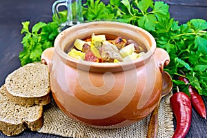 Roast meat and vegetables in clay pot on dark board