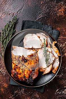 Roast rolled pork ham meat on plate with thyme. Dark background. Top view