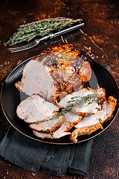 Roast rolled pork ham meat on plate with thyme. Dark background. Top view