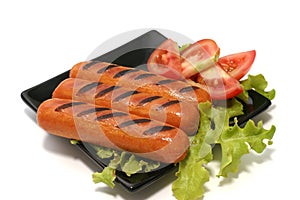 Roast sausages on black dish with tomatoes