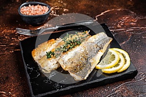 Roast sea bass fillet with lemon and thyme, seabass fish. Dark background. Top view