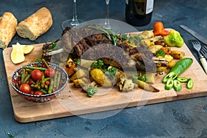 Roast shoulder of lamb on baked potato and carrots, wooden board, top view