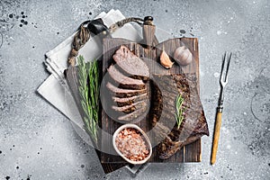 Roast and sliced tri tip beef steak on a wooden board with herbs. Gray background. Top view