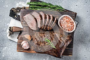 Roast and sliced tri tip beef steak on a wooden board with herbs. Gray background. Top view