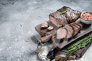 Roast and sliced tri tip beef steak on a wooden board with herbs. Gray background. Top view. Copy space