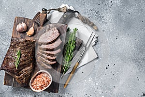 Roast and sliced tri tip beef steak on a wooden board with herbs. Gray background. Top view. Copy space