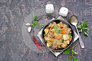 Roast, stewed beef with potatoes and carrots in a brown clay bowl on a dark concrete background
