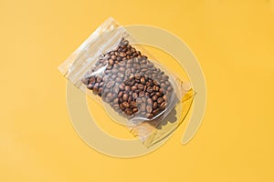 Roasted arabica coffee beans in blank transparent plastic bag with zipper on yellow background. Specialty and alternative sample